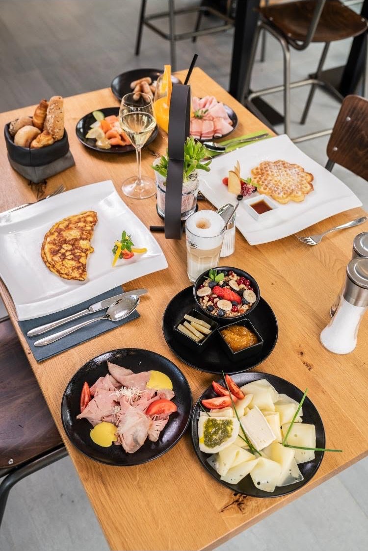 Reich gedeckter Frühstückstisch mit Omelette, Waffeln, Aufschnitt, Käse und Müsli-Bowl