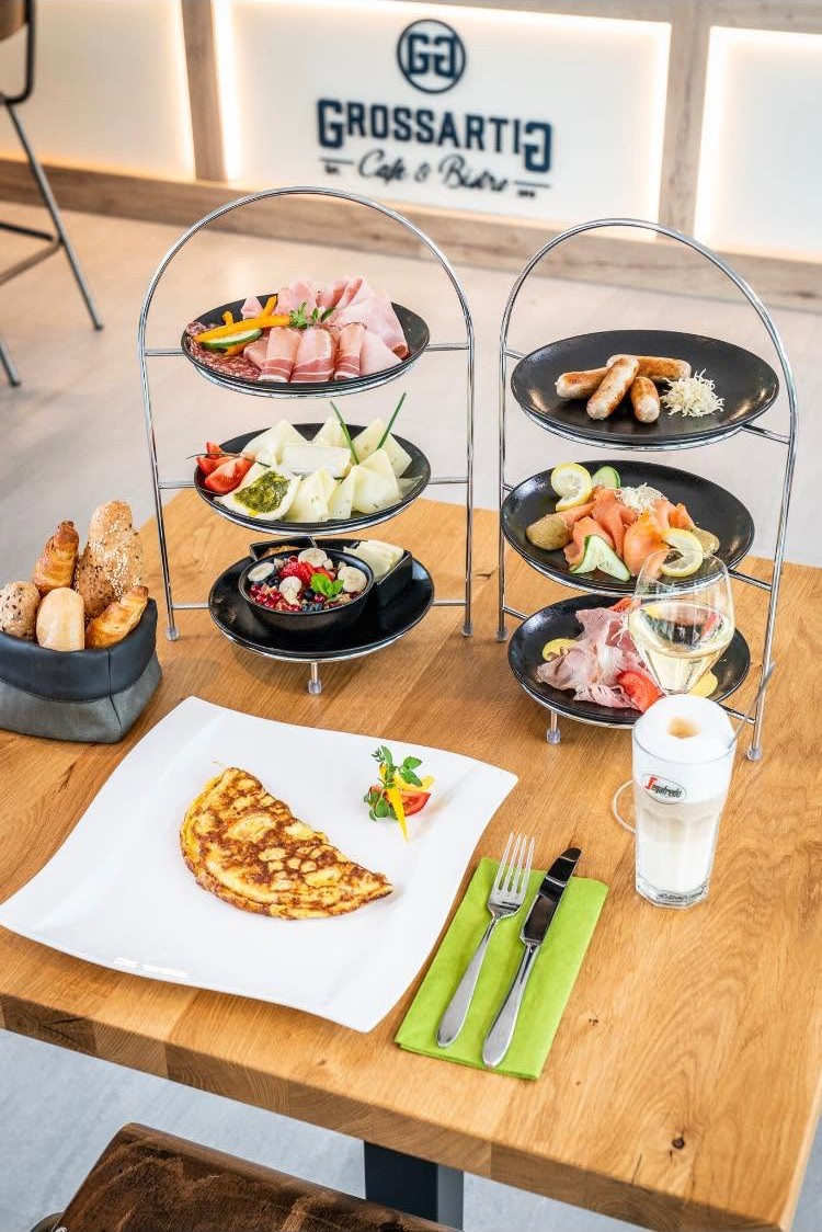 Zwei Etageren mit Schinken, Käse, Würstchen, Lachs, Obst und Gebäck, dazu Omelette und Latte macchiato
