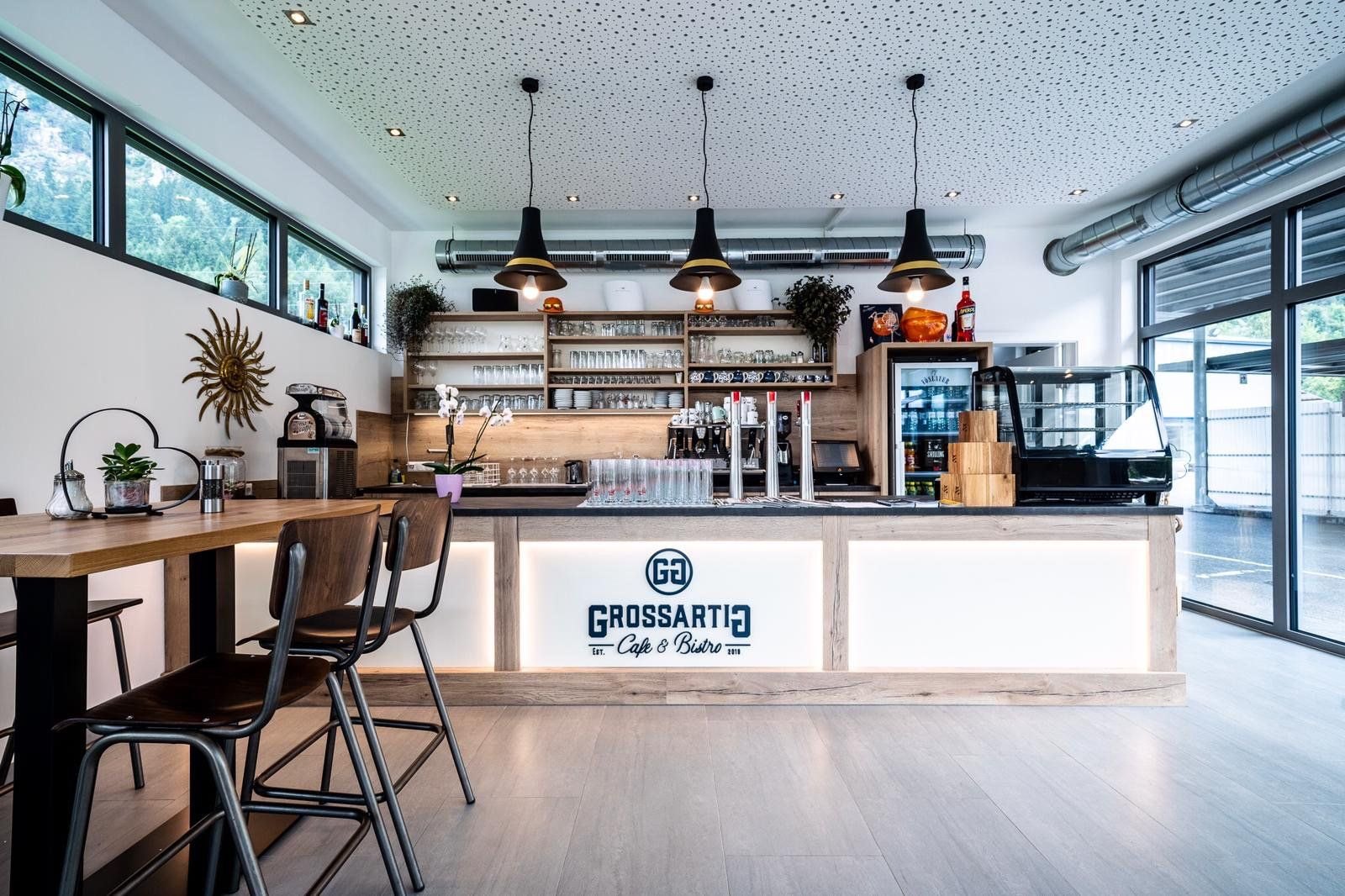 Die beleuchtete Theke des Café & Bistro Grossartig mit Logo, Glasregalen und Pendelleuchten