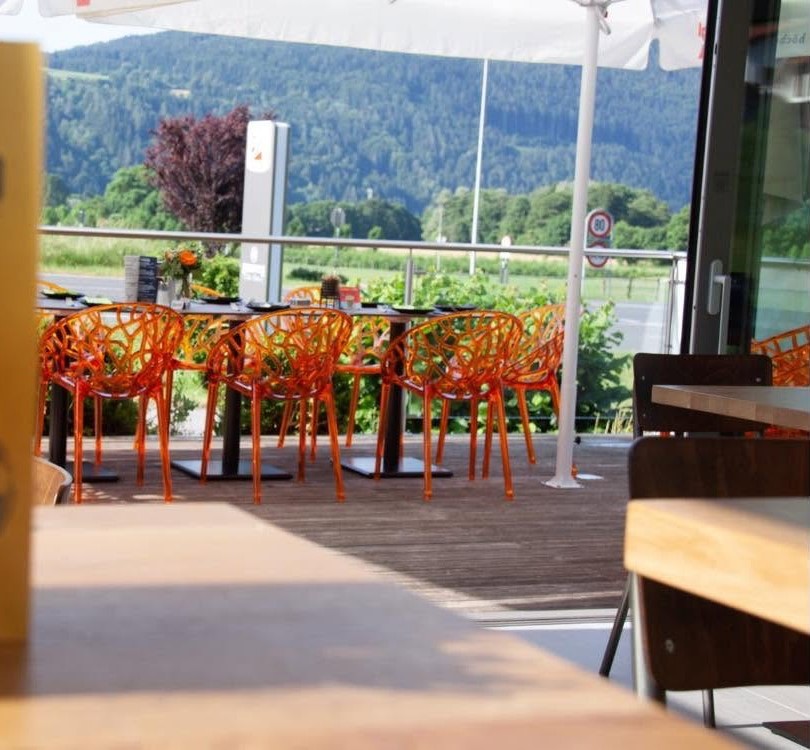 Terrasse mit orangen Designsesseln und Blick auf die bewaldeten Hänge
