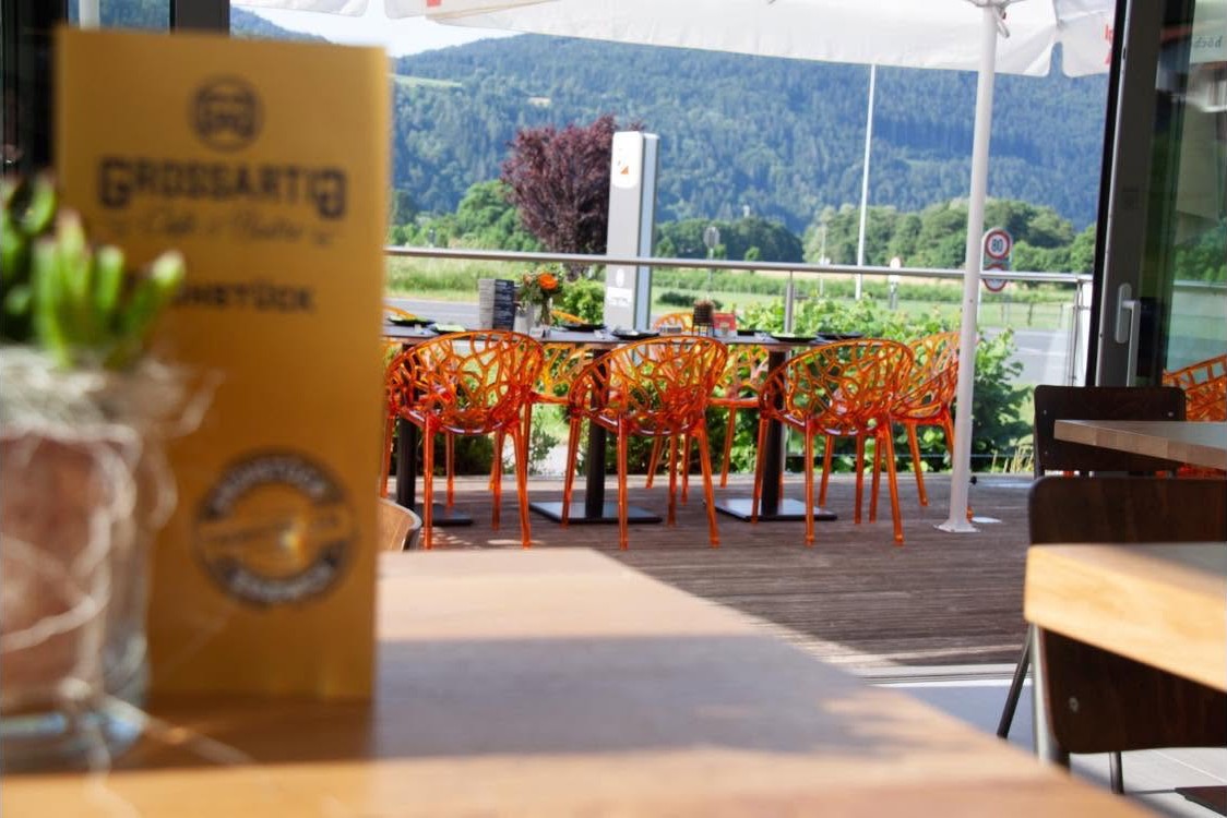Blick aus dem Gastraum durch die geöffnete Front auf die Terrasse mit orangen Sesseln